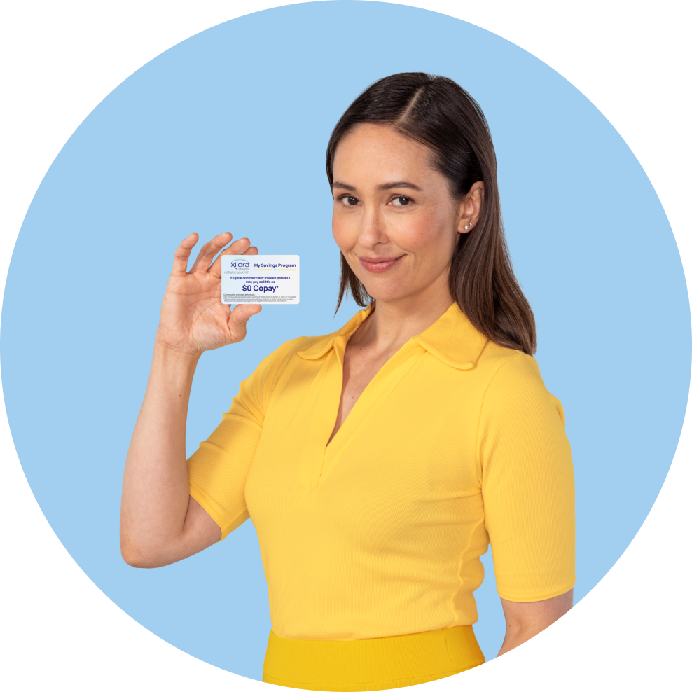 White woman with brown hair in a yellow outfit holds up a Xiidra Savings Program card
